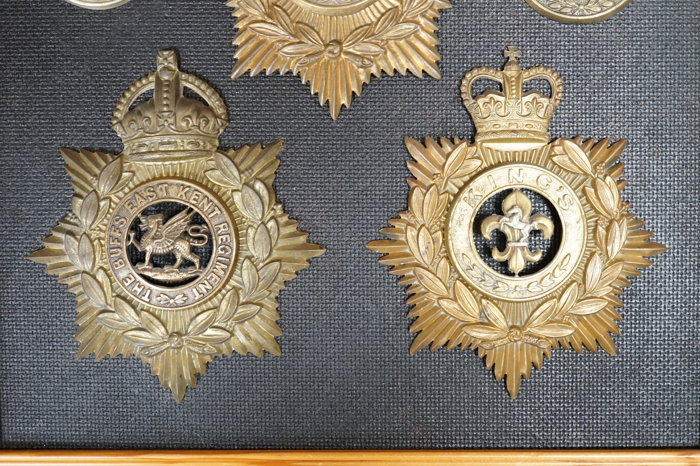 Five military helmet plates and two other centre badges, mounted on a board including; the Essex Regiment, the North Staffordshire 1st Volunteer Battalion, the Somerset Regiment, the Buffs East Kent Regiment, the King’s